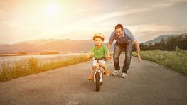 Kind auf Fahrrad mit Papa im Hintergrund
