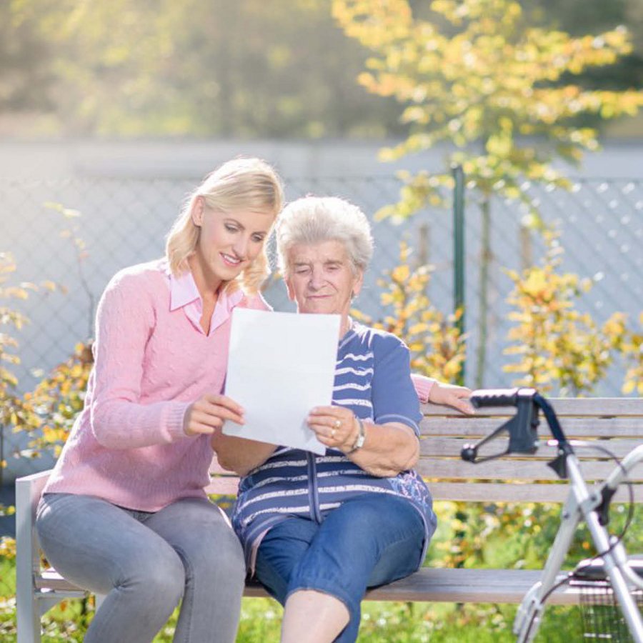 ältere Dame schaut sich mit junger Frau draußen ein Bild an